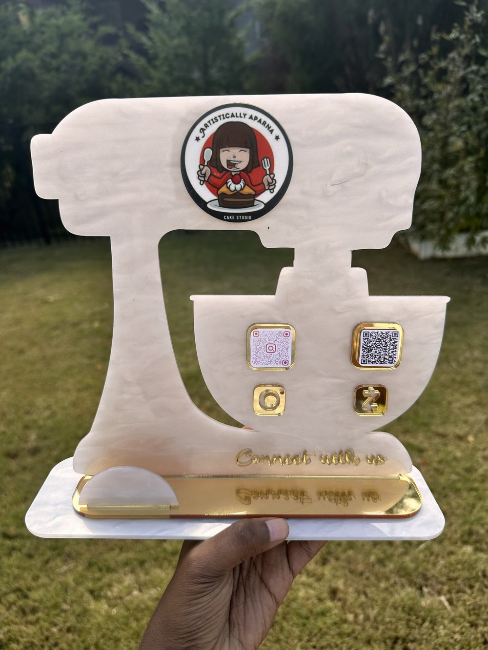 Marble white acrylic QR sign stand shaped like a stand mixer, held outdoors