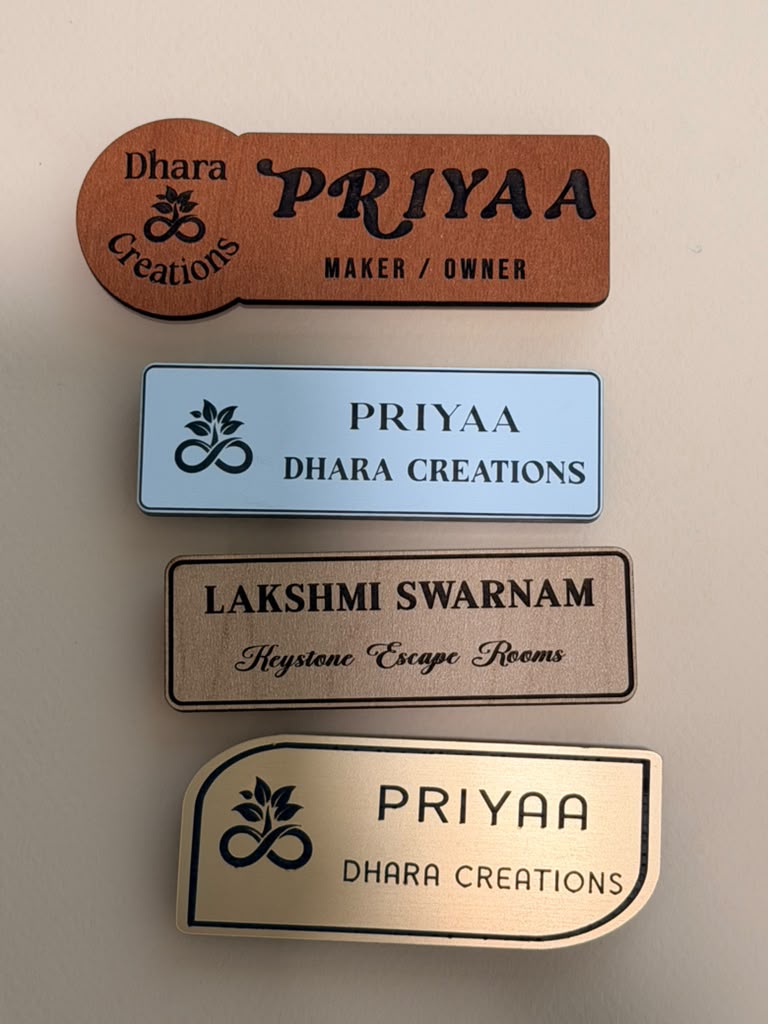 Four custom name badges in wood, blue acrylic, brushed metal, and silver metallic finishes
