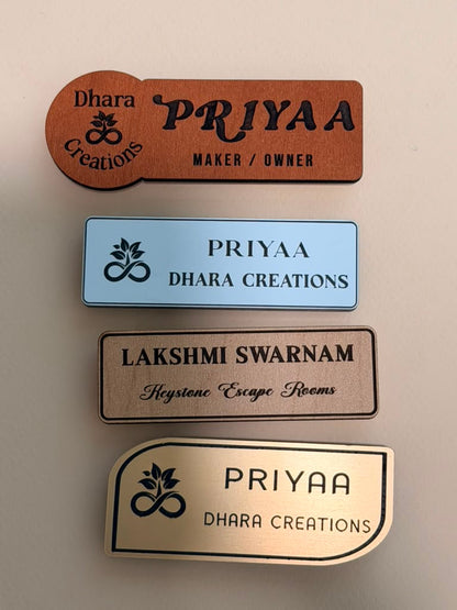 Four custom name badges in wood, blue acrylic, brushed metal, and silver metallic finishes