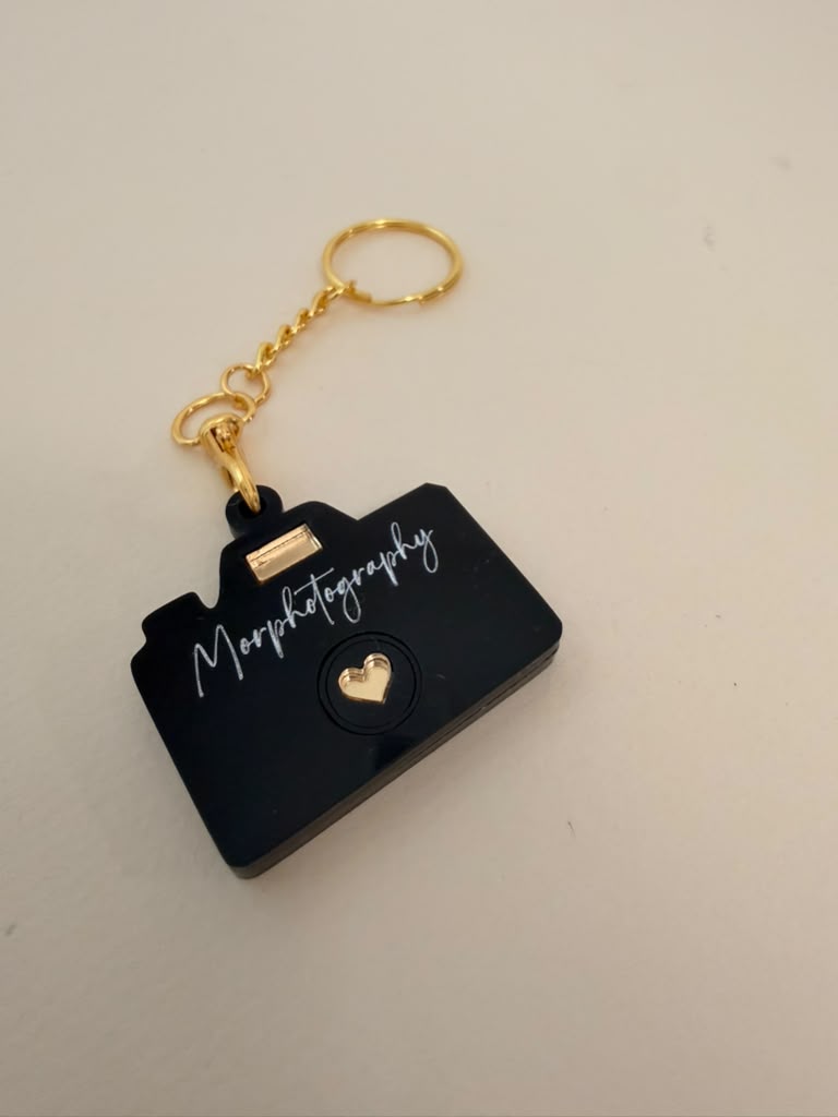 Black acrylic camera-shaped keychain with Morphotography engraved in white script