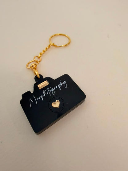 Black acrylic camera-shaped keychain with Morphotography engraved in white script